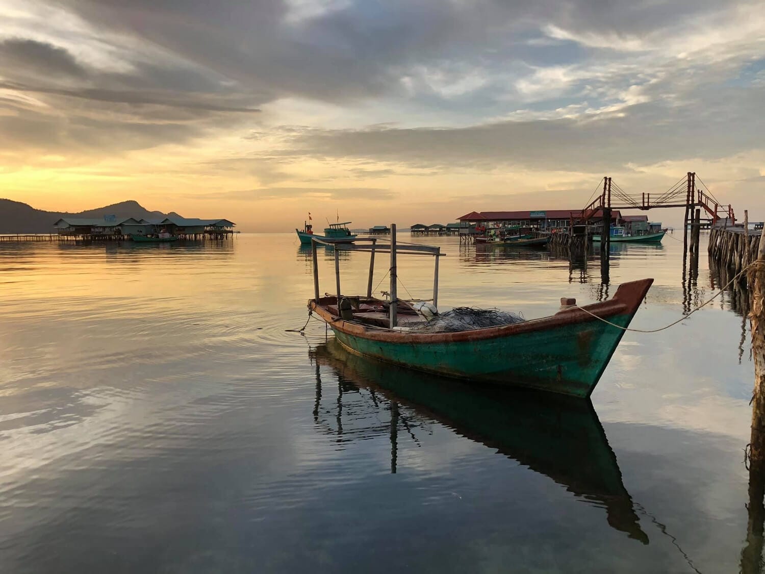 A small wooden boat anchored near a raft house at Rach Vem Fishing Village, clear sea water showing many red starfish