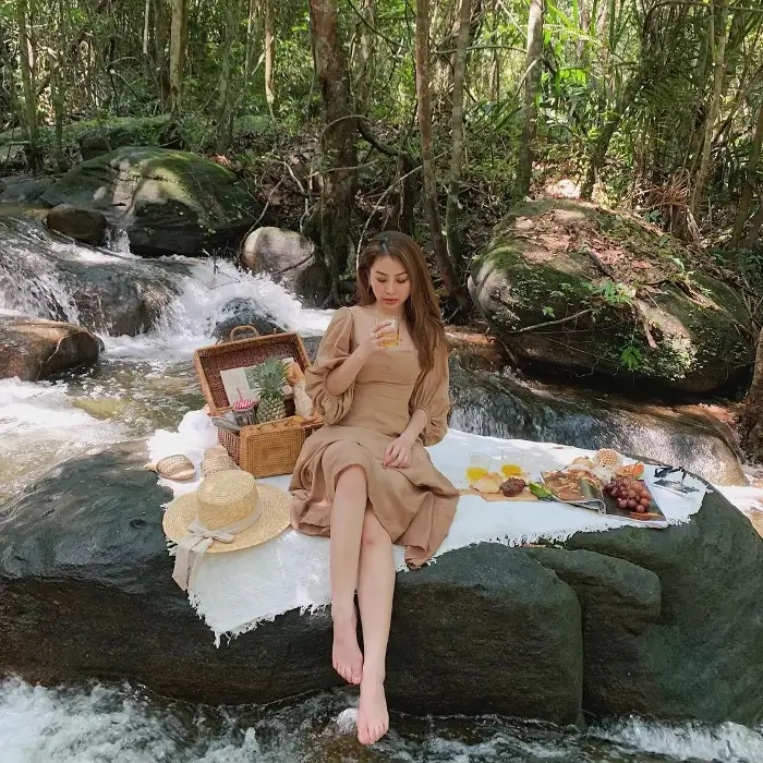 Du khách ngồi thư giãn bên bàn picnic trên phiến đá, xung quanh là dòng suối chảy giữa rừng nguyên sinh Suối Mây Phú Quốc