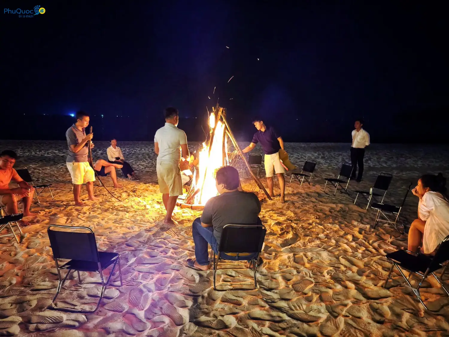 Group of tourists gathering around a campfire on Vinh Dam Phu Quoc sandy beach at night