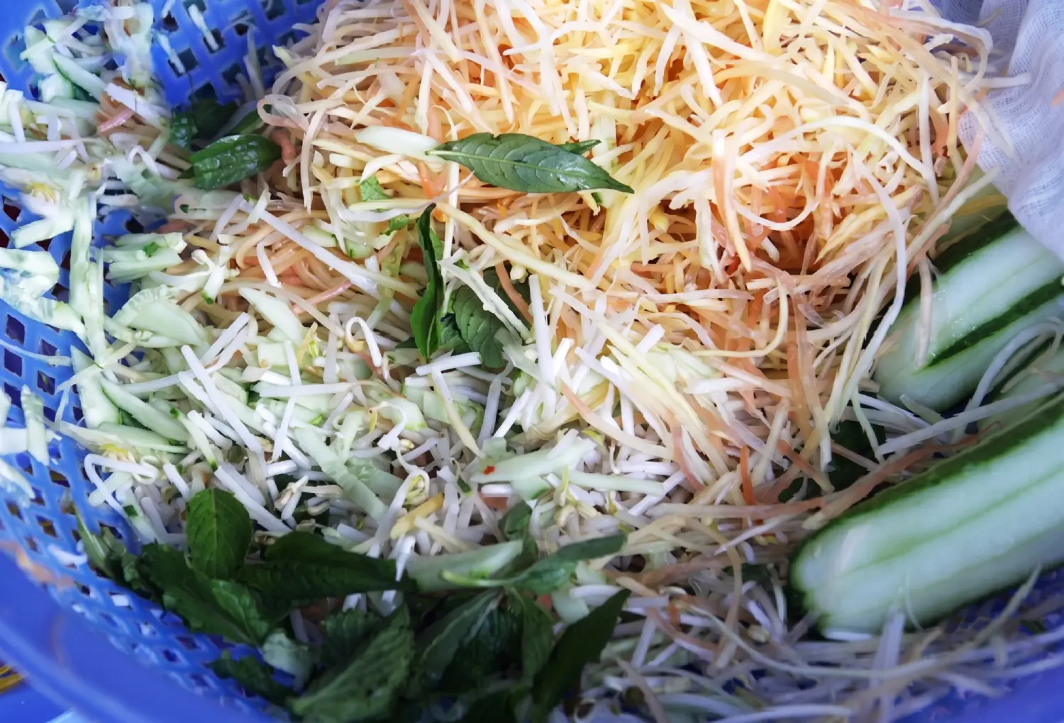 Fresh green vegetables such as shredded green papaya, sliced cucumber, and herbs prepared